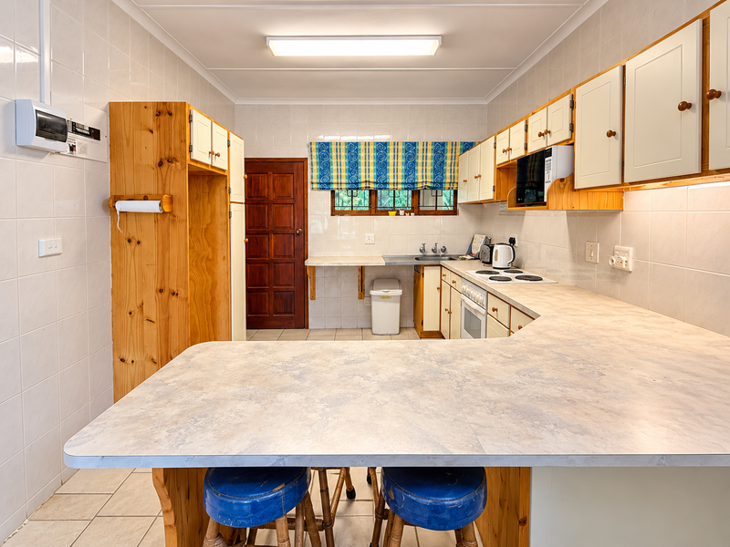 A functional kitchen featuring tiled walls and flooring, ample built-in cabinetry, a breakfast counter, and integrated cooking appliances.