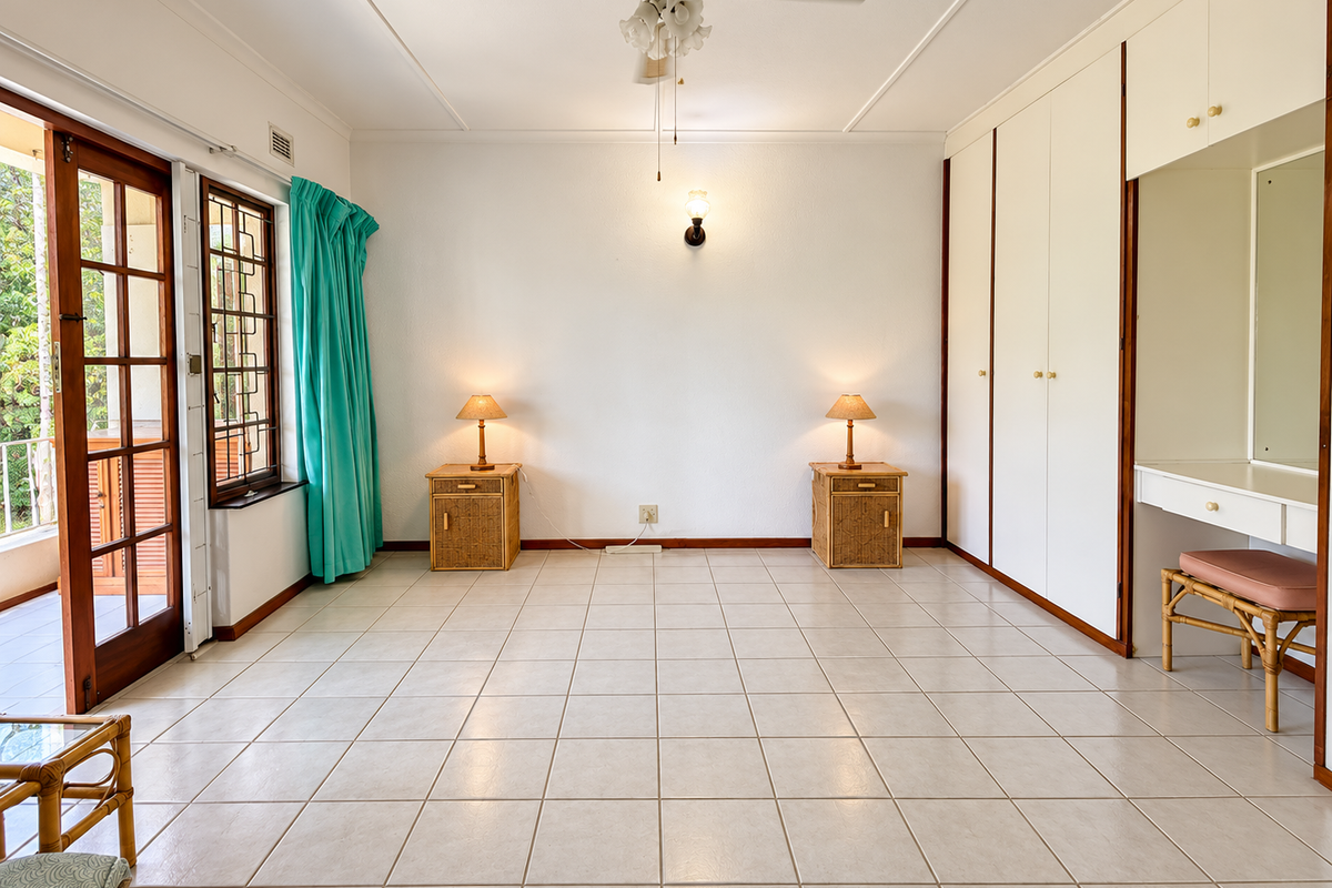 Spacious bedroom featuring built-in cupboards, a vanity unit, tiled flooring, and direct access to an outdoor balcony through timber-framed glass doors.