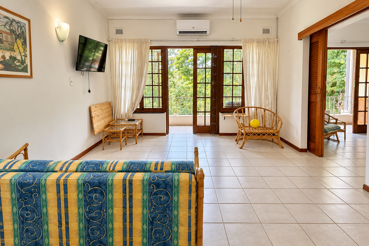 Spacious living area featuring tiled flooring, air conditioning, and large wooden doors opening onto a balcony, providing ample natural light.