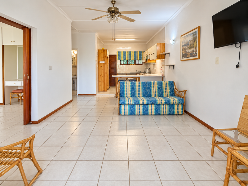Open-plan living and kitchen area featuring tiled flooring, a ceiling fan, and functional kitchen cabinetry with a breakfast bar.