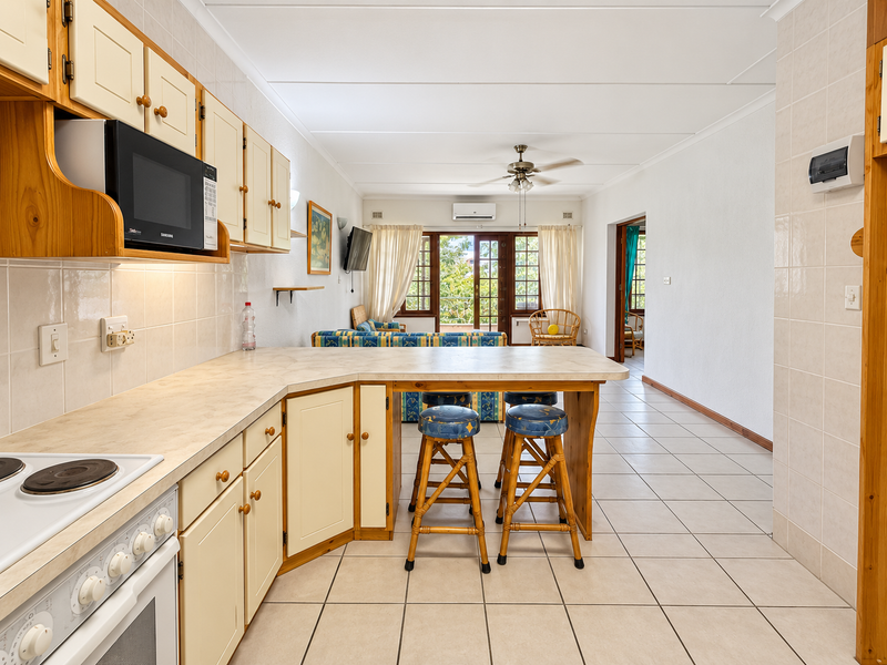 Open-plan kitchen and living area featuring tiled flooring, built-in cabinetry, integrated appliances, and direct access to a balcony through sliding glass doors.