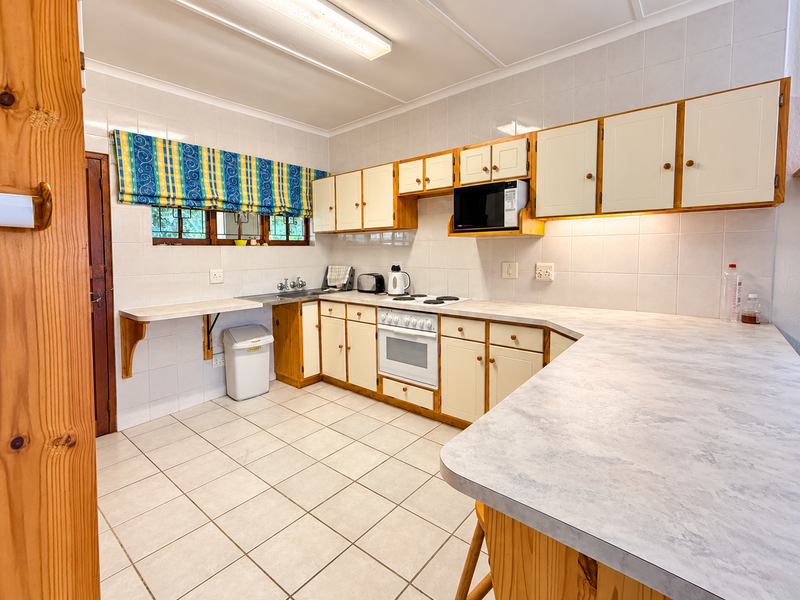 A functional kitchen featuring ample built-in cabinetry, laminate countertops, a ceramic tile backsplash, and tiled flooring, offering a practical layout for daily use.