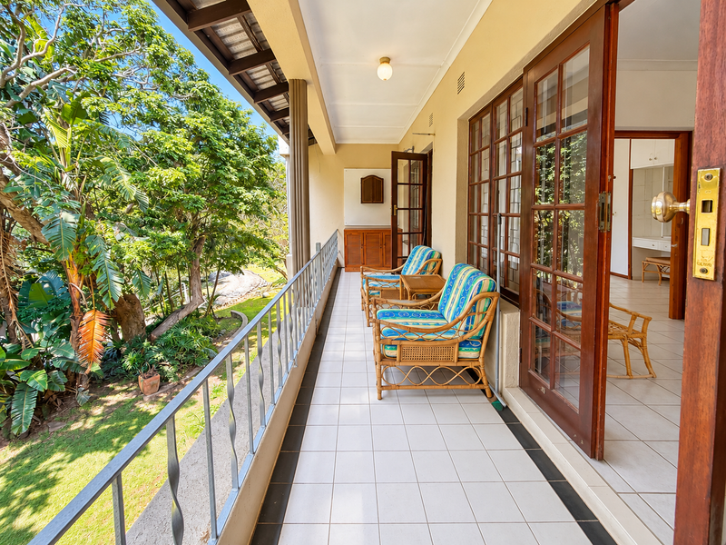 A spacious covered balcony featuring tiled flooring, a metal balustrade, and wooden framed glass doors providing access to the interior living space.