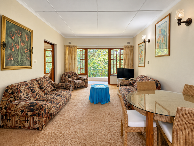 Spacious open-plan living and dining area featuring carpeted floors, classic wall lighting, and direct access to a balcony through wooden casement doors.
