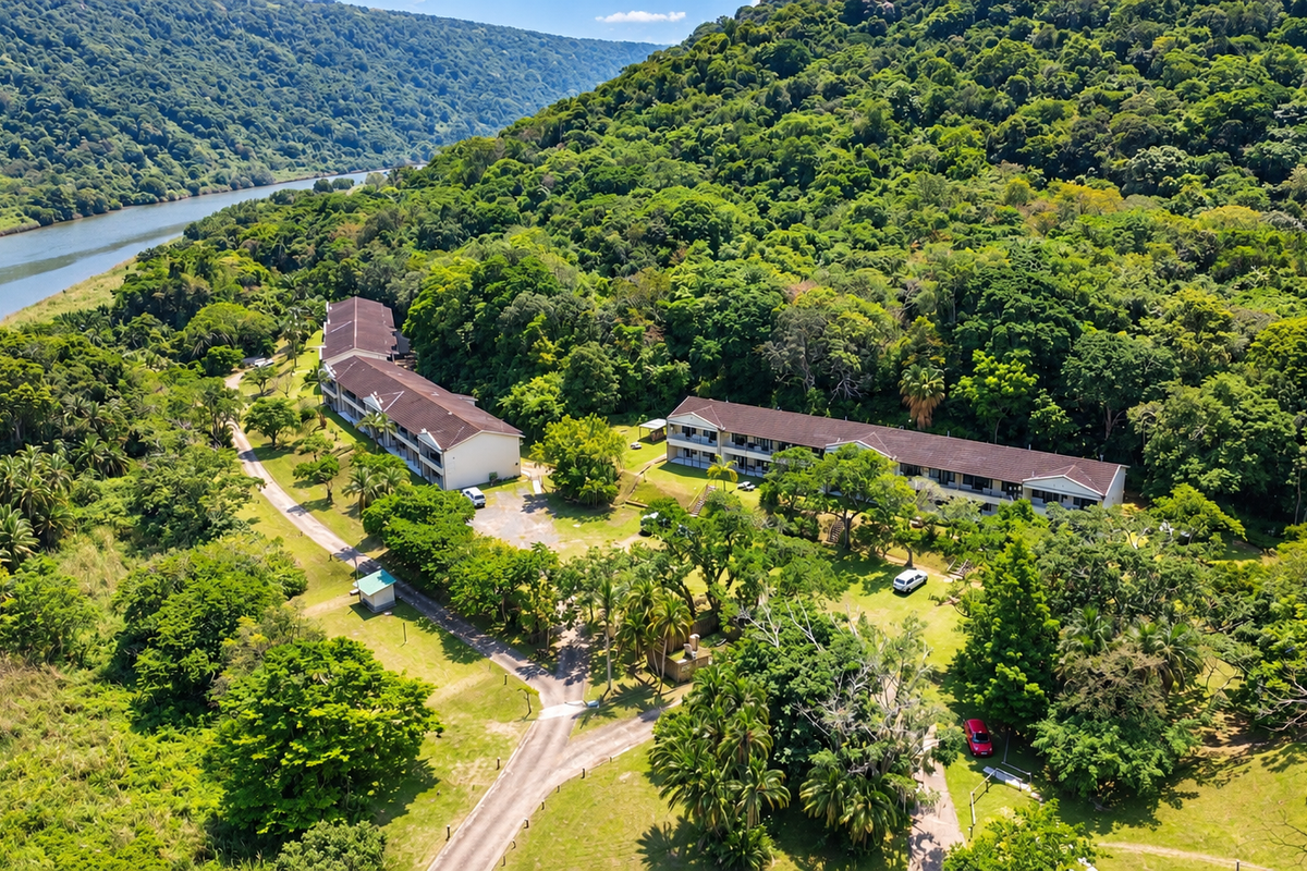Aerial view of a residential apartment complex situated in a lush, green landscape with direct river frontage and extensive natural surroundings.