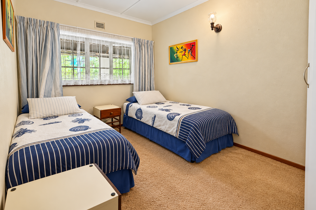 A functional bedroom featuring carpeted flooring, a window with security bars, and a wall-mounted light fixture.