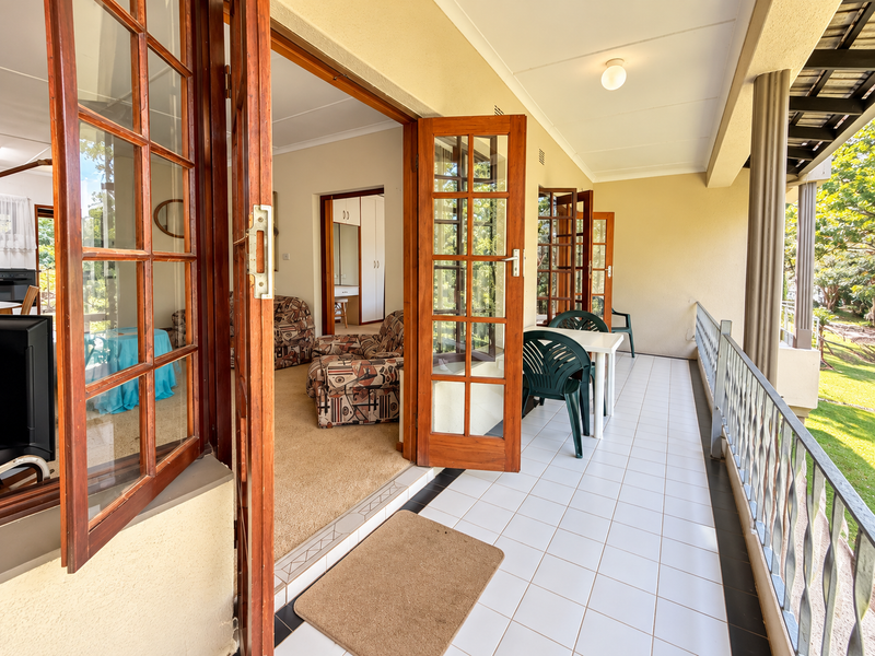 A spacious covered balcony featuring tiled flooring, a metal balustrade, and multiple wooden french doors providing access to the interior living area.