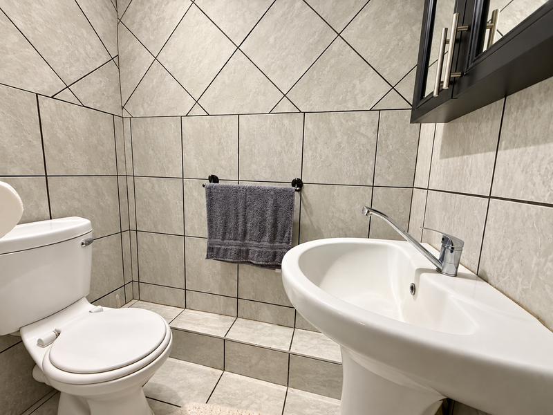 A compact bathroom featuring a pedestal sink, toilet, and full-height ceramic wall tiling with a neutral finish.