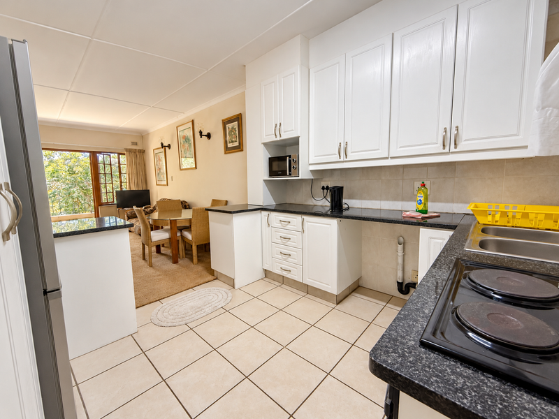 Open-plan kitchen and dining area featuring white cabinetry, granite countertops, electric hob, and tiled flooring, leading to a balcony.