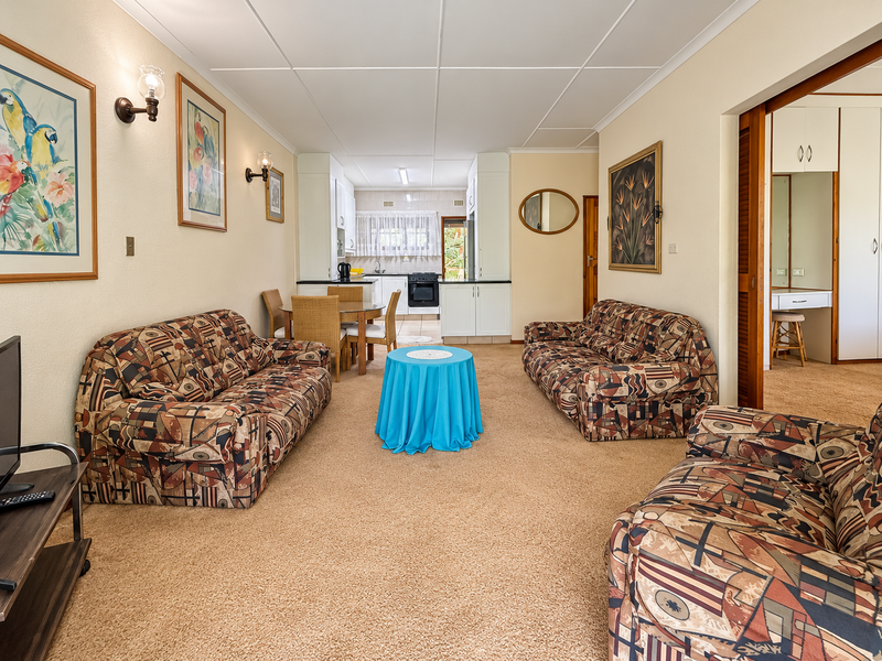 Open-plan living and dining area featuring carpeted floors, connected to a functional kitchen with built-in cabinetry and a freestanding stove.