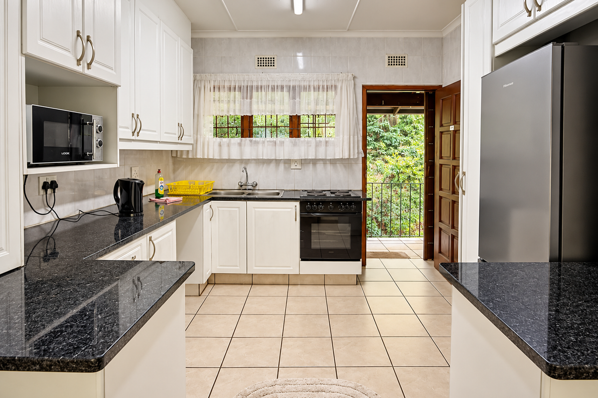 A functional kitchen featuring white cabinetry, dark granite countertops, built-in oven and hob, tiled flooring, and direct access to an outdoor balcony area.