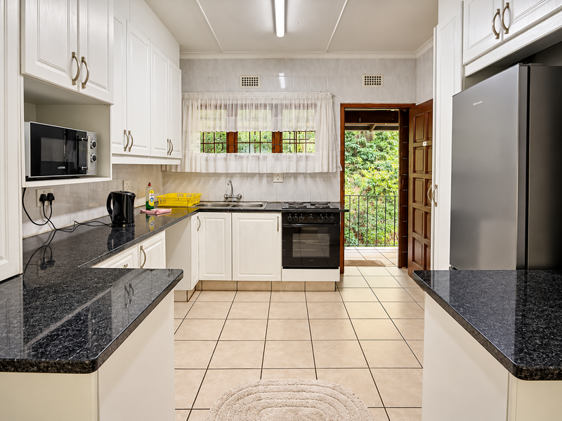 A functional kitchen featuring white cabinetry, dark granite countertops, built-in oven and hob, tiled flooring, and direct access to an outdoor balcony area.