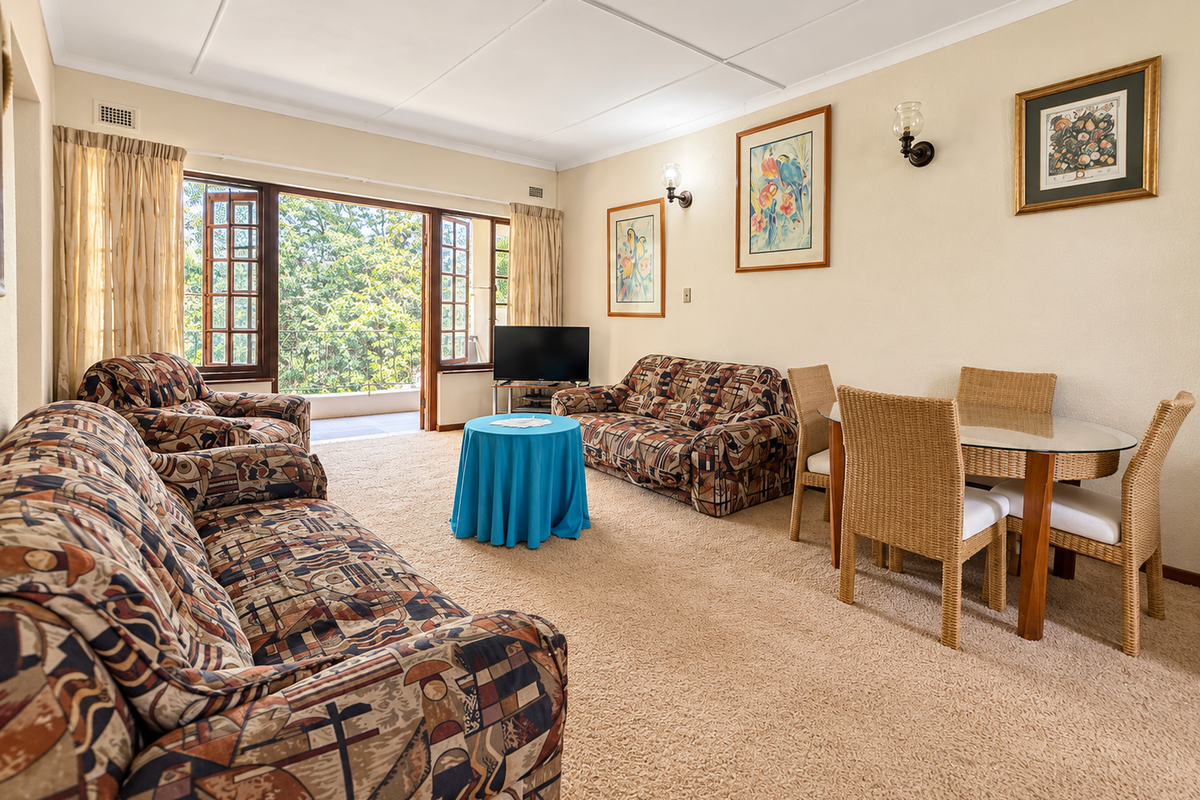 Spacious living room featuring carpeted flooring, wall sconces, and large wooden-framed glass doors opening onto a balcony.