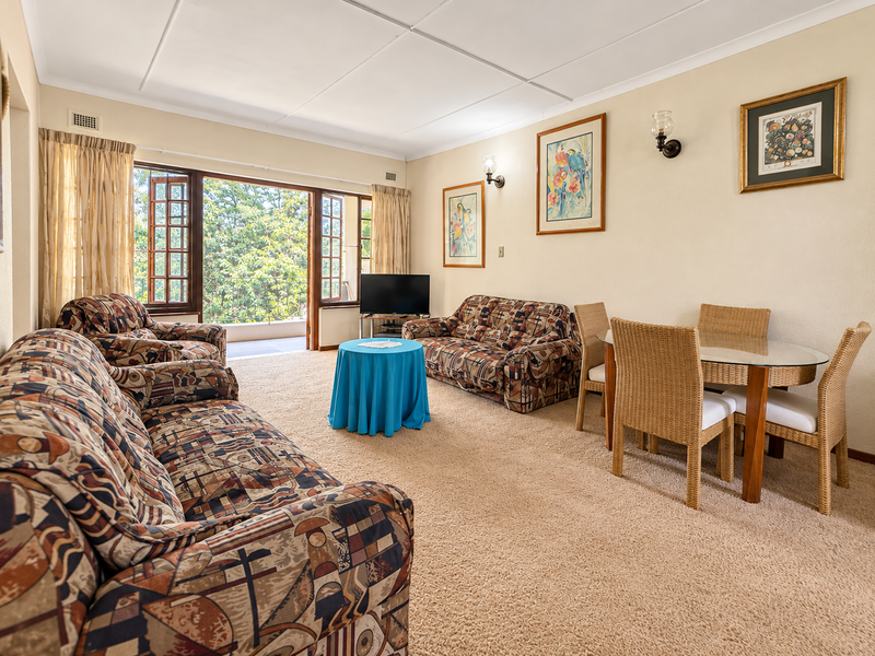 Spacious living room featuring carpeted flooring, wall sconces, and large wooden-framed glass doors opening onto a balcony.