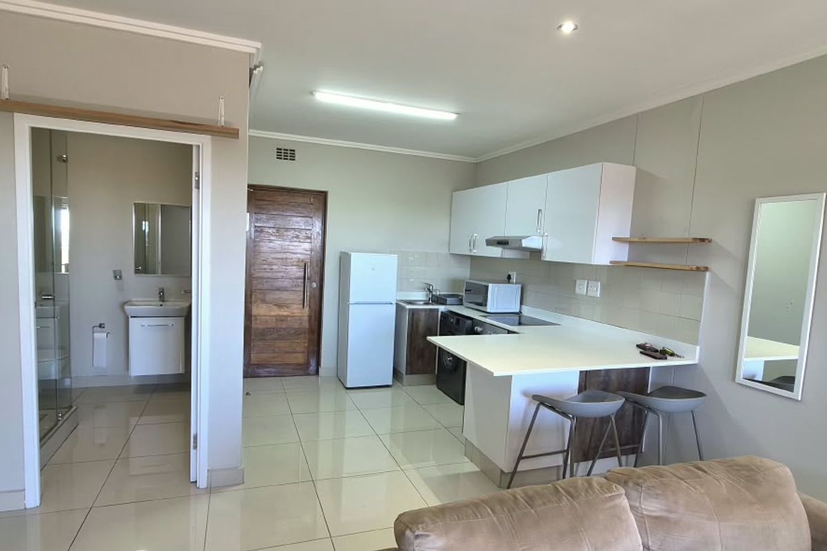 An open-plan living area featuring a modern kitchen with white cabinetry, a breakfast bar, and tiled flooring, with direct access to an adjacent bathroom.