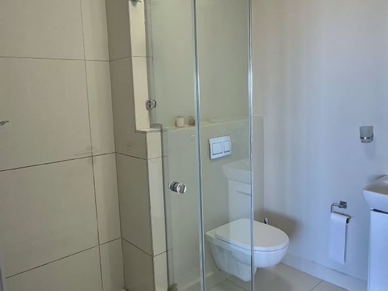 Modern bathroom featuring a glass-enclosed shower, wall-mounted toilet with concealed cistern, and neutral floor-to-ceiling tiling.