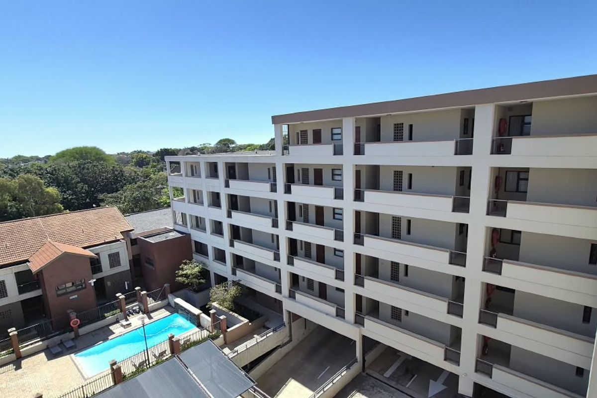 An elevated aerial view of the apartment complex, showcasing the building facade, balconies, parking area, and communal swimming pool.