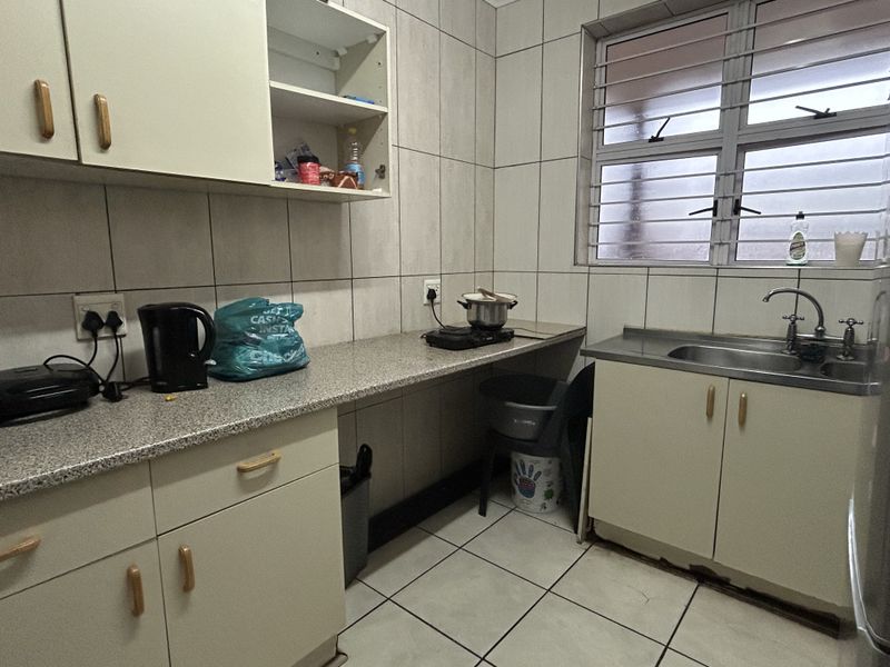A functional kitchen featuring tiled walls and floors, laminate countertops, and built-in cabinetry with a stainless steel sink and security-barred window.