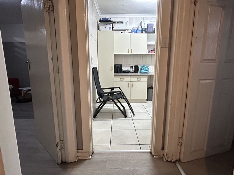 A compact scullery or utility area featuring built-in cabinetry, tiled flooring, and a tiled splashback, viewed from an adjacent hallway.