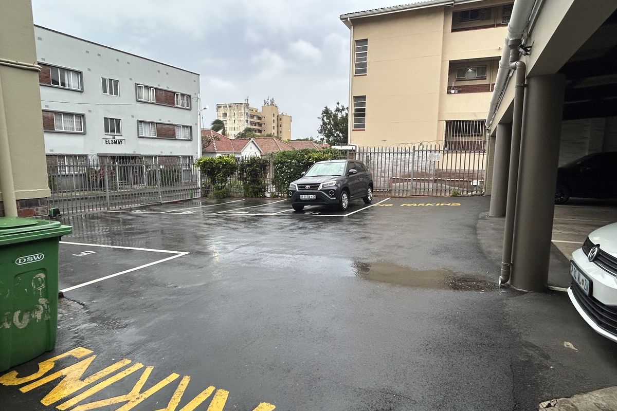 An outdoor parking area featuring asphalt surfacing, marked parking bays, and secure perimeter fencing within an apartment complex setting.