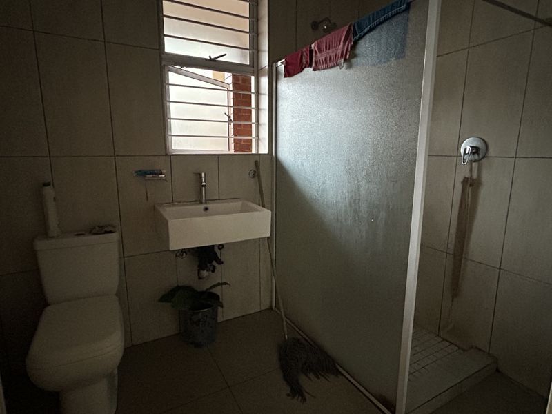A functional bathroom featuring a wall-mounted basin, toilet, and a shower enclosure with tiled finishes throughout.