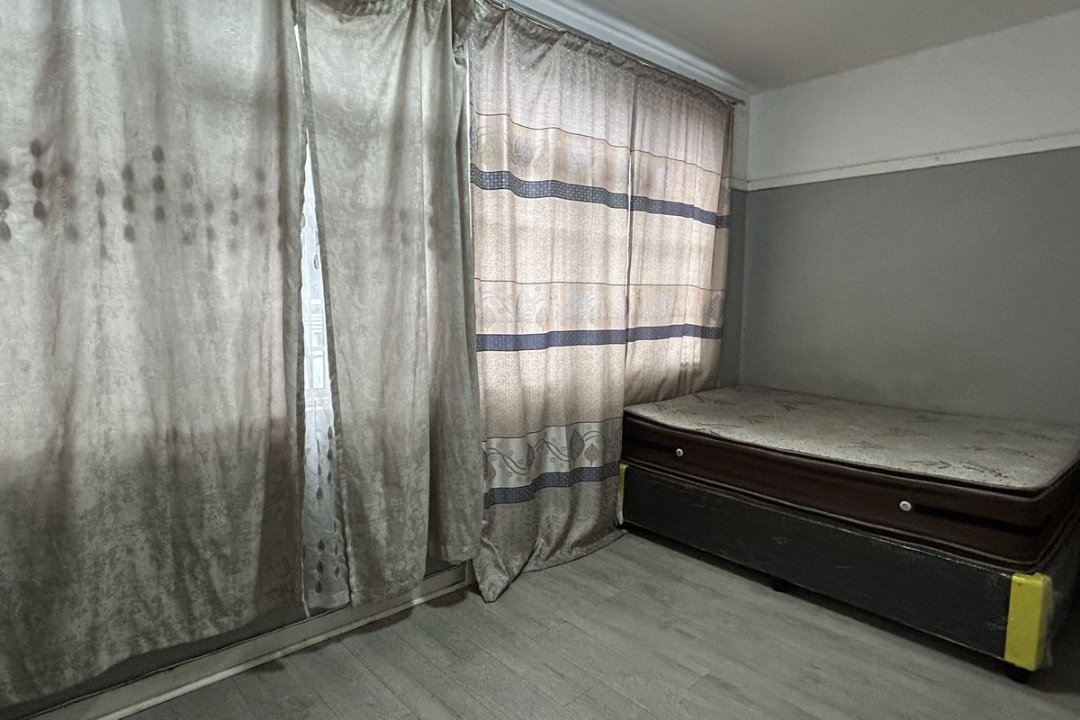 A bedroom featuring laminate flooring and large window curtains, providing a neutral base for personalization.