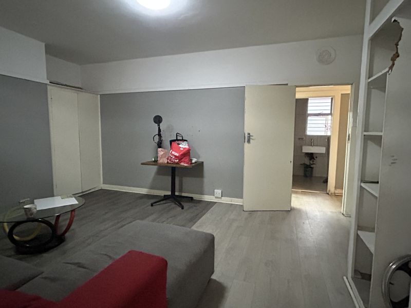 Living area featuring laminate flooring, built-in cupboards, and access to an adjacent bathroom. The space requires cosmetic updates to improve its overall condition.