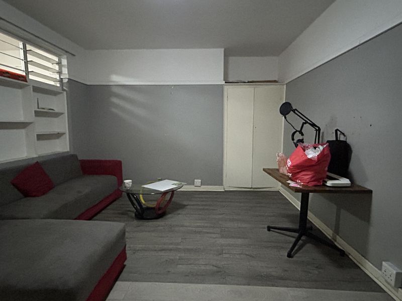 A living room featuring laminate flooring, built-in shelving, and a built-in cupboard, requiring cosmetic updates to improve its overall appeal.