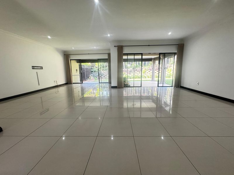 Spacious, light-filled living area featuring large format porcelain tiles, recessed lighting, and expansive sliding glass doors opening to the rear patio and garden.