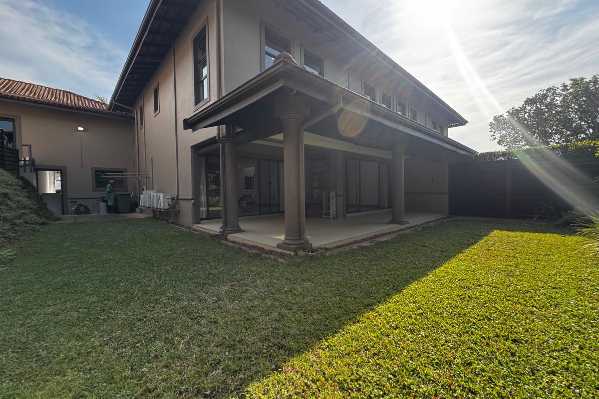 Rear view of the property featuring a spacious covered patio with concrete columns, sliding glass doors, and a well-maintained lawn.