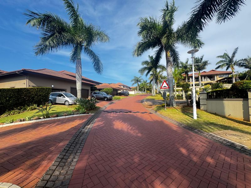 A well-maintained residential street view featuring paved driveways, mature palm trees, and manicured landscaping within a secure estate setting.