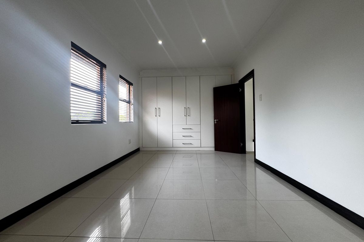 A bright, empty bedroom featuring neutral tiled flooring, built-in cupboards, and modern recessed lighting, offering a clean and versatile living space.