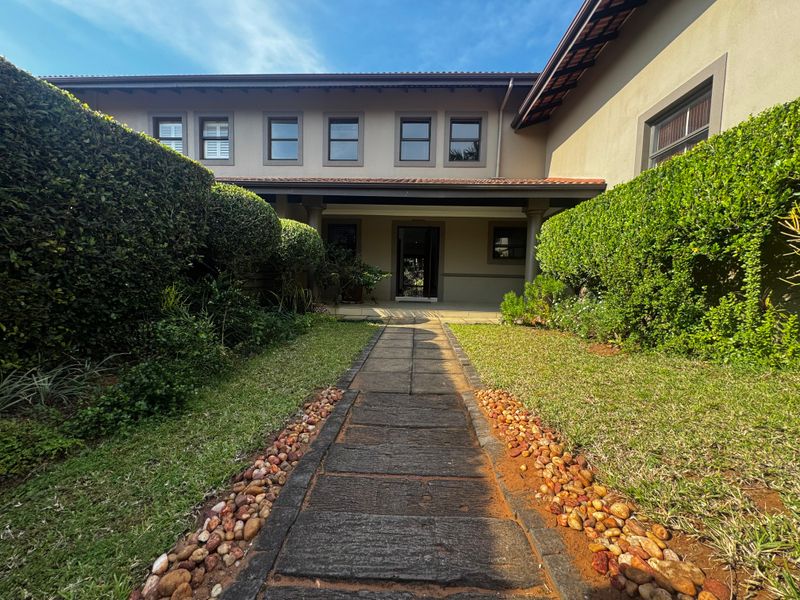 A well-maintained front entrance featuring a paved walkway flanked by manicured hedges leading to a covered porch area.