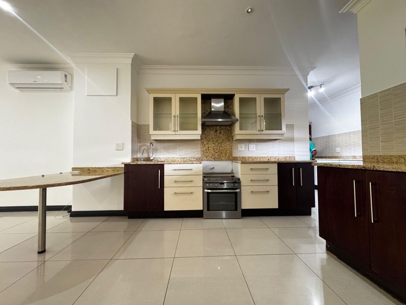 A clean, modern kitchen featuring granite countertops, built-in oven with extractor fan, and ample cabinetry, set against neutral tiled flooring.