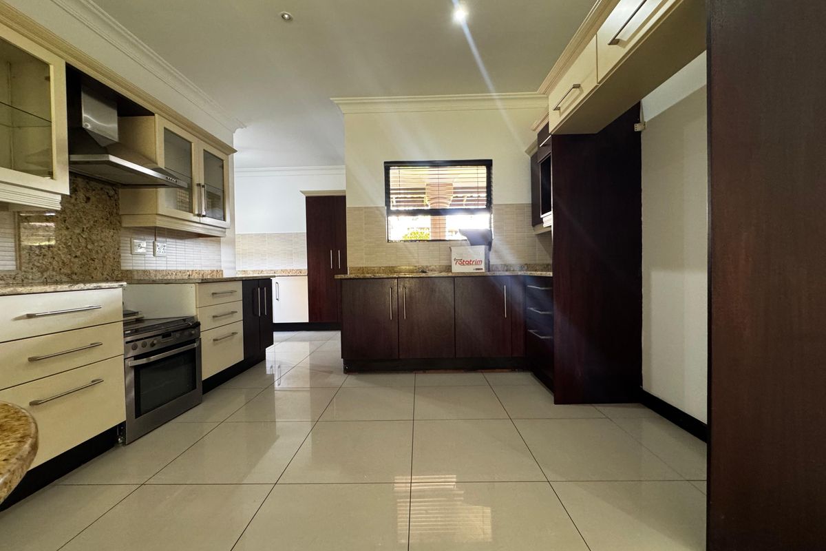 Spacious kitchen featuring granite countertops, built-in cabinetry, and a built-in oven with extractor fan, finished with modern tiled flooring.
