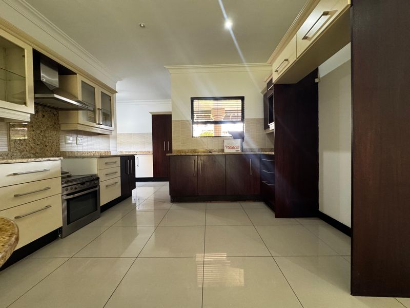 Spacious kitchen featuring granite countertops, built-in cabinetry, and a built-in oven with extractor fan, finished with modern tiled flooring.