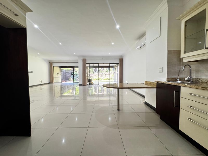 Spacious open-plan living and kitchen area featuring polished porcelain tiles, modern cabinetry, granite countertops, and large sliding doors leading to the outdoor patio.