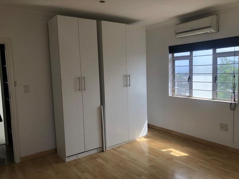A bright, empty bedroom featuring light laminate flooring, built-in white cupboards, and a wall-mounted air conditioning unit.