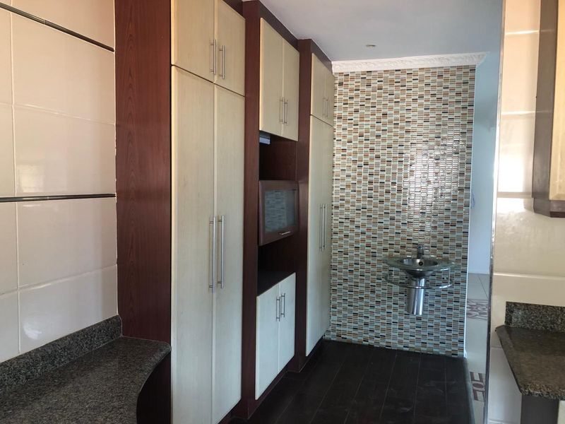 A functional scullery area featuring built-in cabinetry, granite countertops, and a modern wall-mounted basin with a decorative mosaic tile feature wall.