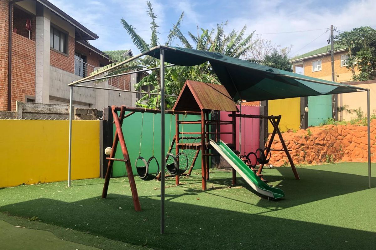 A communal garden area featuring artificial turf, a shaded playground structure, and perimeter boundary walls.