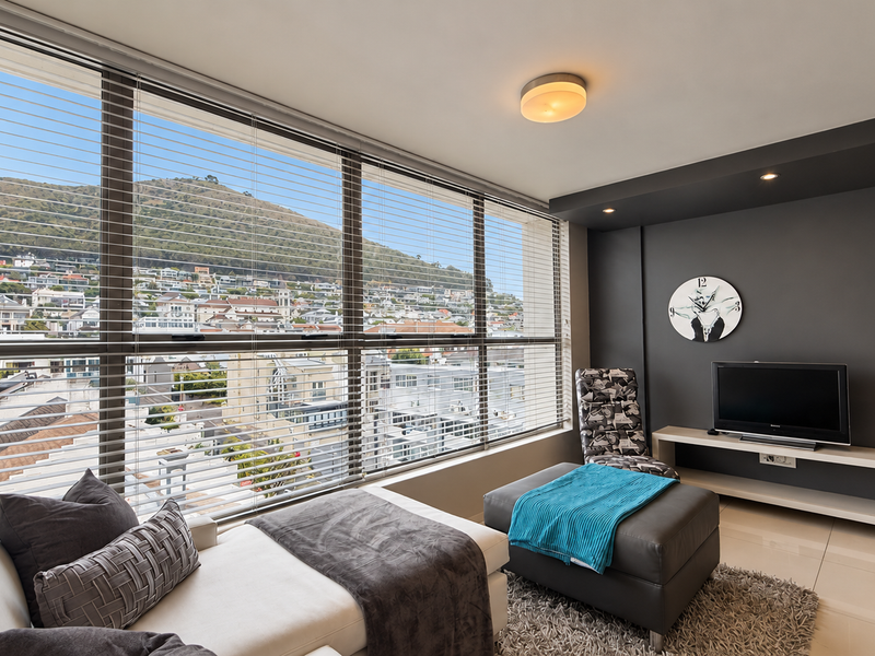 A bright and modern living area featuring large floor-to-ceiling windows with expansive urban and mountain views, complemented by sleek tiled flooring and an accent wall.