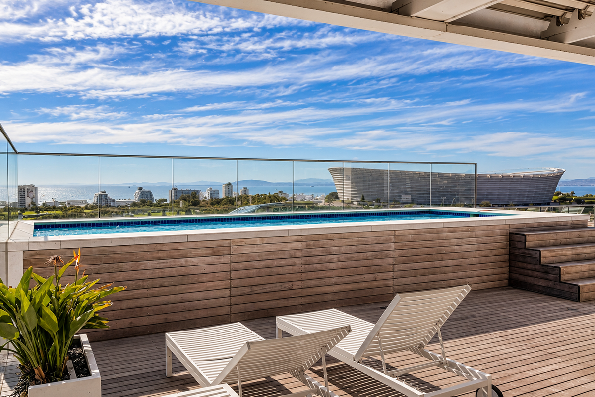 A stunning elevated swimming pool on a timber deck balcony, featuring a glass balustrade and panoramic city and ocean views.