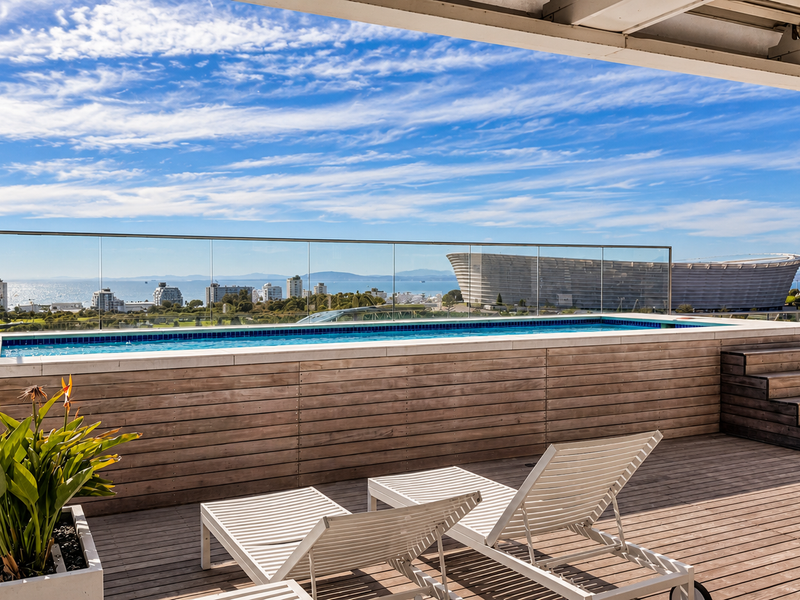 A stunning elevated swimming pool on a timber deck balcony, featuring a glass balustrade and panoramic city and ocean views.
