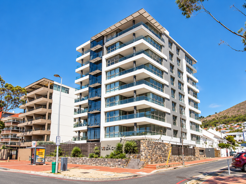 Modern multi-story apartment building featuring glass balconies, stone cladding, and a contemporary architectural design situated on a corner lot.