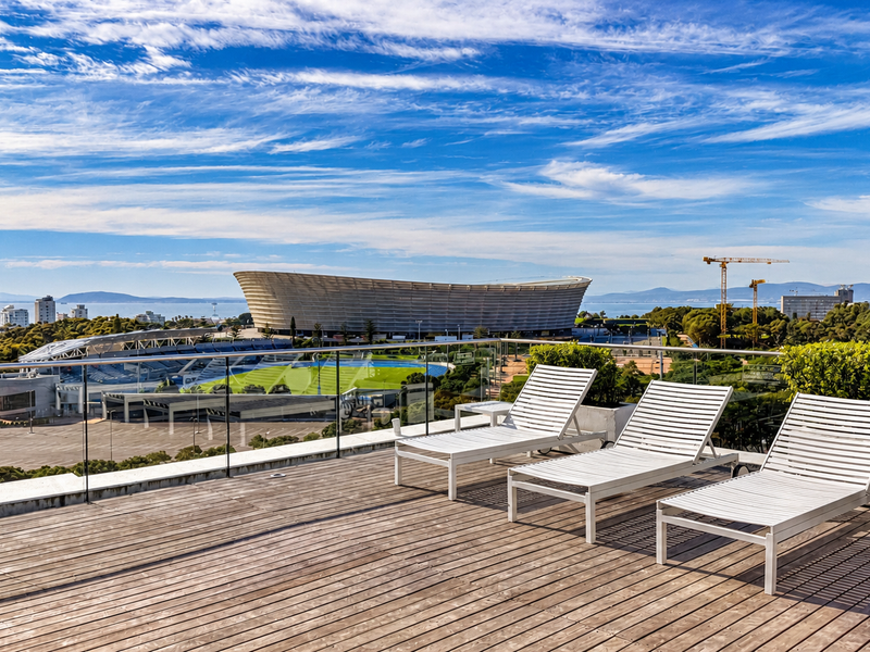 Spacious balcony featuring timber decking and a modern glass balustrade, offering expansive views of the stadium and surrounding landscape.