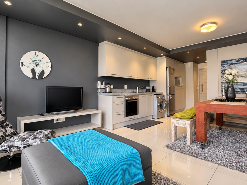Modern open-plan living area featuring a sleek kitchen with built-in cabinetry, granite countertops, integrated appliances, and polished tiled flooring throughout.
