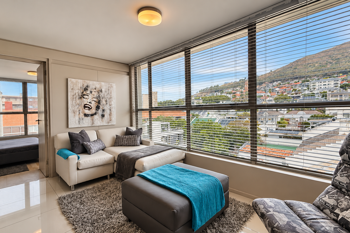 Bright living area featuring large floor-to-ceiling windows with venetian blinds, offering expansive urban and mountain views, complemented by polished tiled flooring.