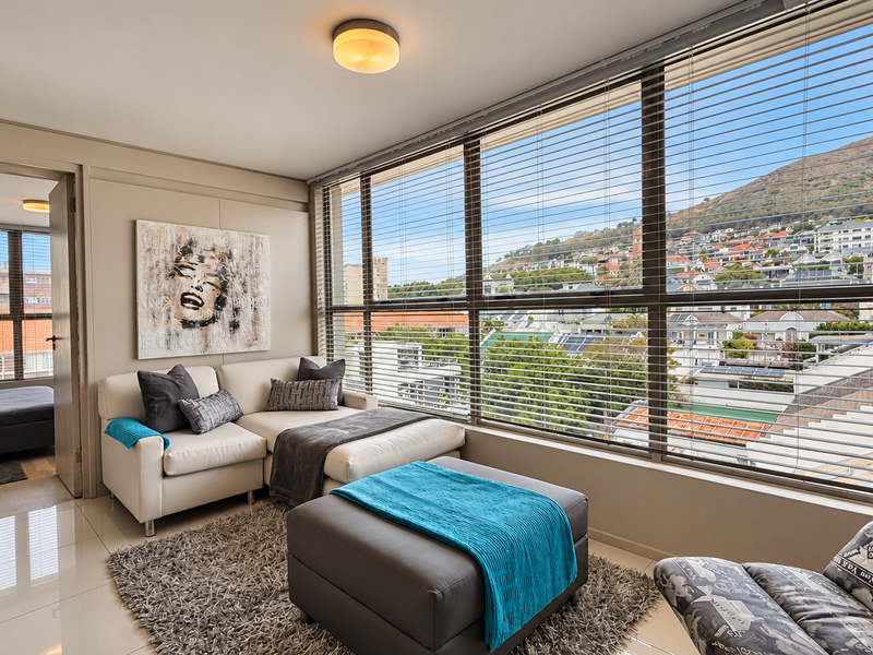 Bright living area featuring large floor-to-ceiling windows with venetian blinds, offering expansive urban and mountain views, complemented by polished tiled flooring.