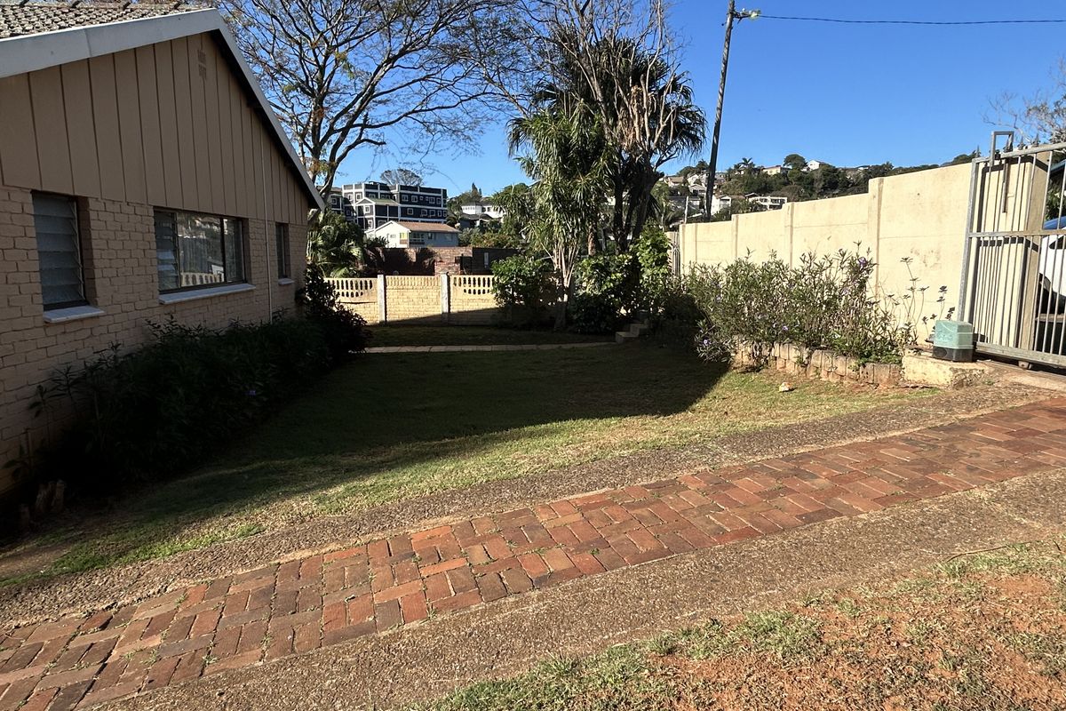 A rear garden area featuring a brick driveway, precast concrete boundary walls, and a metal sliding gate, providing access to the side of the house.