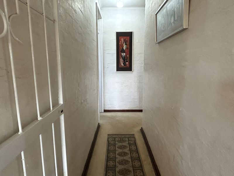 A narrow interior hallway featuring painted brick walls, a security gate, and standard skirting boards.